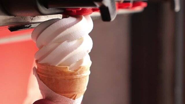 Soft serve vanilla ice cream flowing into crispy wafer cone from dispenser machine in slow motion close up