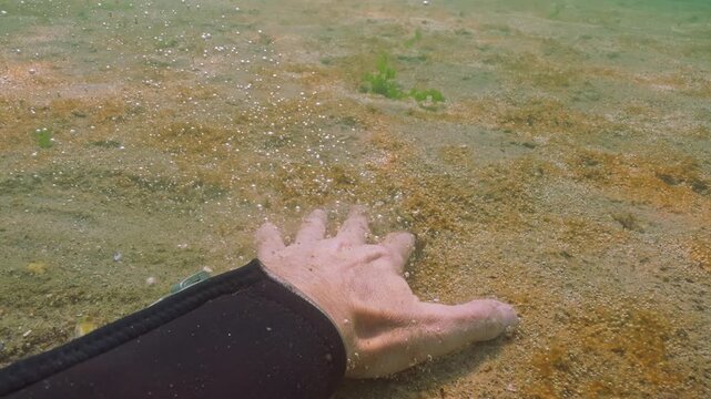 First person view: Men's hand slides into side of sandy bottom and rips off thin biofilm of microalgae colonies that release gas, causing many small bubbles to float up. POV shot, slow motion