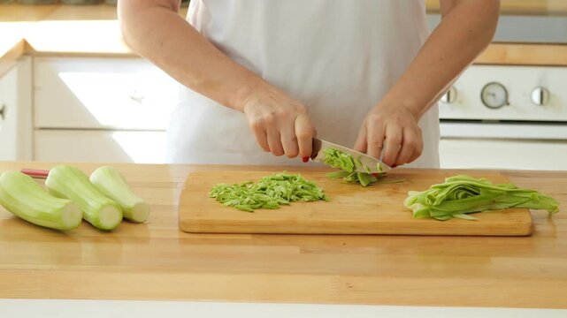 Person is cutting celery on a wooden cutting board. The celery is cut into small pieces