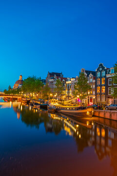 Illuminated boats and houses at Ronde Lutherse Kerk on Singel canal during twilight, Amsterdam, Netherlands