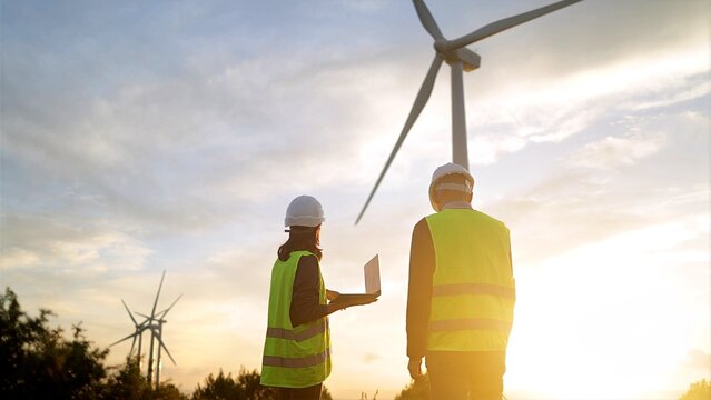 At sunset on a wind farm, engineers wearing safety vests work together to examine wind turbines, strategizing for sustainable energy growth and overseeing performance