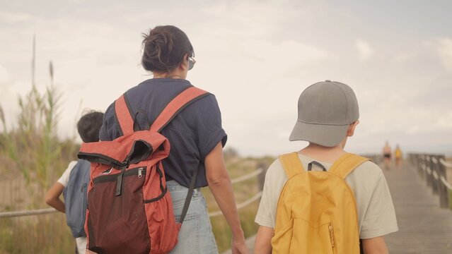 Mother and children walking on a wooden boardwalk, exploring a nature reserve near the beach during a family vacation, enjoying togetherness and outdoor travel