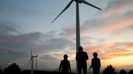 Family admiring wind turbines at sunset, sharing a moment while discussing clean energy, environmental protection, and a sustainable future for younger generations © DawDunia
