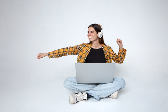 Mujer joven con auriculares y port&aacute;til en el regazo sonriendo celebrando