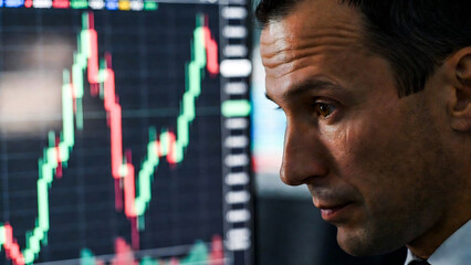 Fototapeta premium A man intently watches a fluctuating stock market graph on a bright screen. He appears focused and serious.