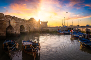 Sunset over Essaouira harbor, Morocco, with blue fishing boats and historic ramparts