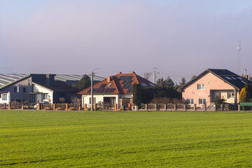 Fototapeta premium Residential houses featuring solar panels on roofs, bordering a vibrant green field, symbolizing sustainable energy and suburban development