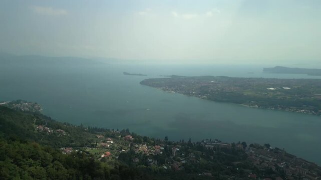 Drone yaw pan over Lake Garda and Salo bay in Lombardy Italy, camera rotates left to right above the waterfront revealing terracotta roofs marina piers and calm blue water