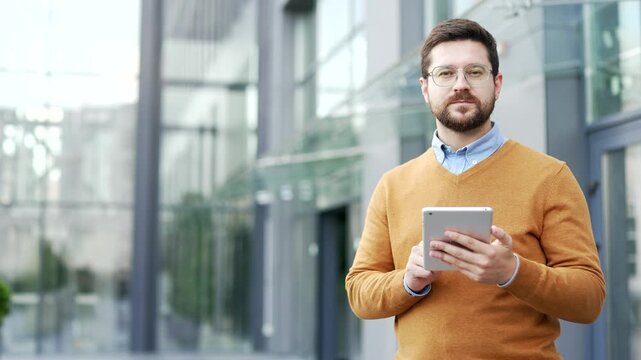 Portrait of confident businessman holding digital tablet standing on street near office building. Male worker looking at camera outdoors. Empty copy space for writing text. Template for advertising
