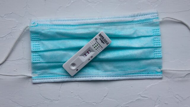 SARS-CoV-2 rapid antigen test with two colored lines - positive result of coronavirus infection and face mask