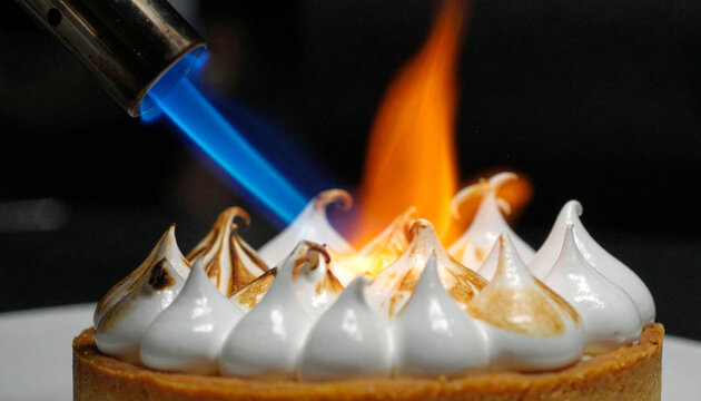 Chef hands using culinary blowtorch to toast glossy meringue on lemon tart