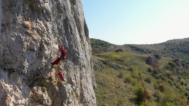   Aerial view of mountain rescuer rappelling on a rocky wall hanging on a rope
