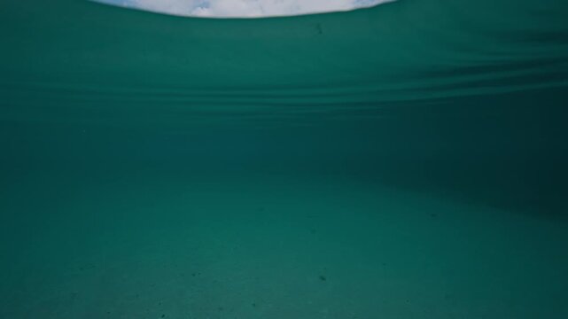 Cinematic split-level transition shot above water with the beach and mountains in view and then smoothly submerging below the surface of the water to reveal the turquoise depths of the ocean