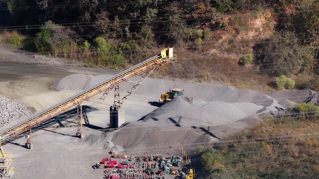 Aerial tracking across conveyor stacker depositing gravel onto stockpile with bulldover pushing and sorting piles