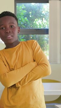 Vertical video: Entering boy in mustard shirt moving to center to pose, crossing arms with desks