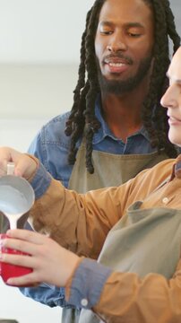 Vertical video: Lifting metal pitcher barista in apron coaching guiding milk pour at cafe, red mug