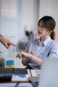 Stressed employee being scolded by boss pointing at watch, tense office confrontation over punctuality, deadlines and accountability in corporate work life