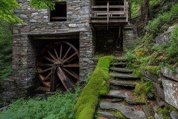 Old stone water mill with a large wooden wheel surrounded by lush greenery and moss-covered stones in a serene natural setting