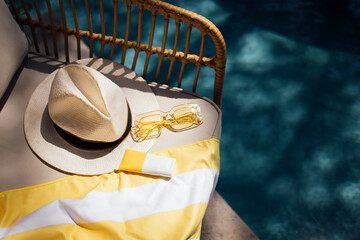 Summer poolside accessories including a straw hat, sunglasses, sunscreen, and a yellow striped...