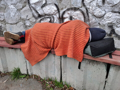 A man covered with a blanket lies on a bench