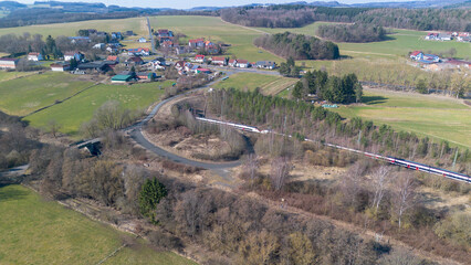 Fototapeta premium Aerial view of passenger train passing tunnel near rural village farmland in Germany