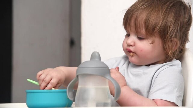 Curious 14-month-old toddler playing with food and sippy cup during mealtime