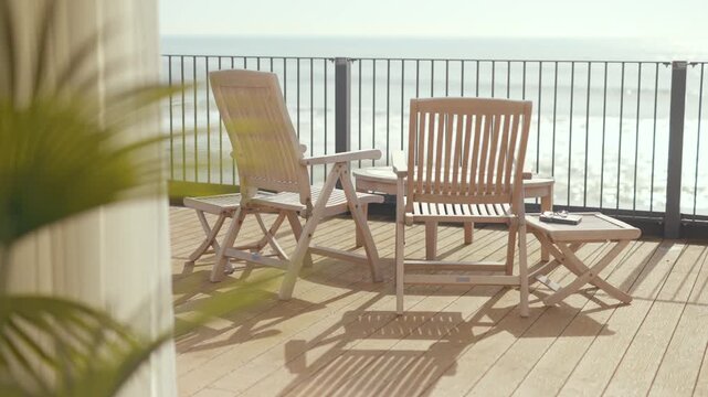 Wooden balcony chairs face ocean horizon. Sunlight warms wooden deck and tray. Morning coffee and flower rest on tray. Peaceful, relaxing seaside morning scene. Ideal for travel, wellness
