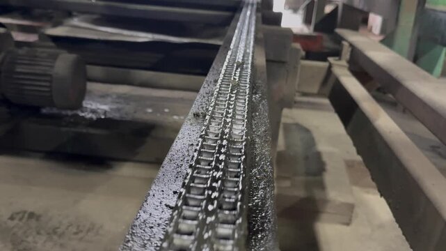 Mechanical drive system in operation, showing a dirty metal roller chain turning gears, heavy industry factory.