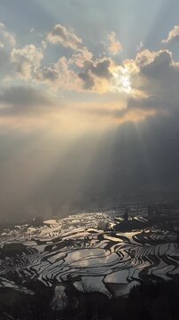 Breathtaking view of sunbeams shining through clouds onto the water-filled Hani rice terraces in Yuanyang, Yunnan, China. A UNESCO World Heritage site.