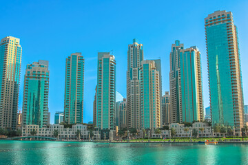 Obraz premium Modern skyscrapers with glass facades lining the vibrant Burj Lake waterfront, depicting rapidly developing urban infrastructure and a luxurious travel destination in the United Arab Emirates