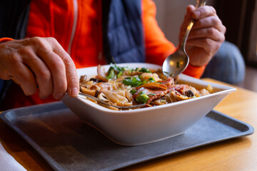 Person eating spicy Asian noodle soup with meat and vegetables in white square bowl, authentic oriental cuisine, hearty lunch at restaurant, close-up delicious food and dining process, Enjoying meal