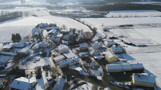 Winter village landscape with snowy fields and rural houses in Bavaria, Germany. Peaceful countryside settlement surrounded by farmland during cold season, filmed from aerial drone perspective.