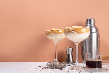 Dalgona espresso martini cocktail with whipped instant coffee and creamy liqueur, viral summer cocktail in two martini glasses, with shaker and bar utensils, copy space