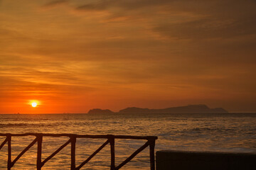 Obraz premium A vibrant summer sunset over the Pacific Ocean along Lima’s Costa Verde, with the silhouette of San Lorenzo Island on the horizon. Warm golden light reflects across the waves