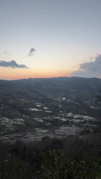 Breathtaking Tyndall effect with sunbeams piercing through clouds onto the water-filled Hani rice terraces at dawn.