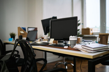 Empty office workspace showing computer monitors, coffee cup, documents, and cleaning supplies on desk, indicating recent or ongoing cleaning process in modern business environment