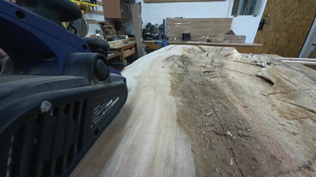 Authentic Faceless Maker Leveling Rough Timber Surface with Power Planer to Prepare Solid Foundation Tracking Shot