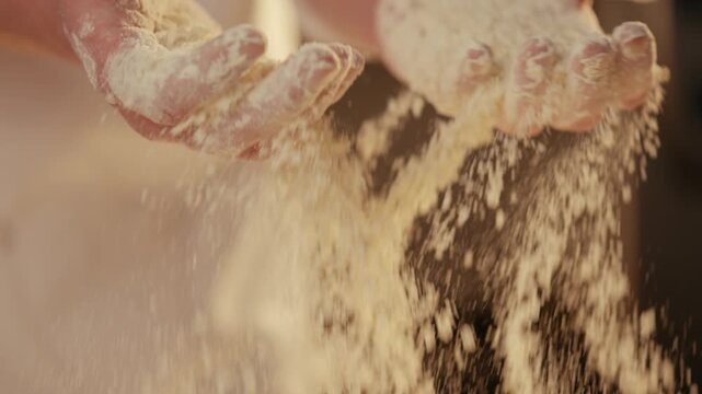 Close-up of flour falling from hands onto a pile. Dust particles float in warm light. Chef's hands dusted with powder show care. Ideal for baking, cooking, or food prep scenes