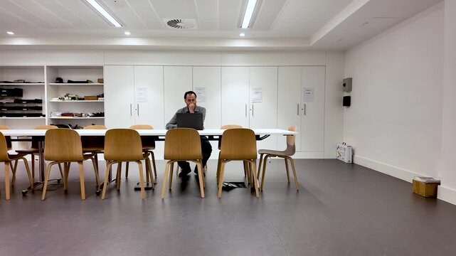 South Asian man working on laptop at a long conference table in an empty office