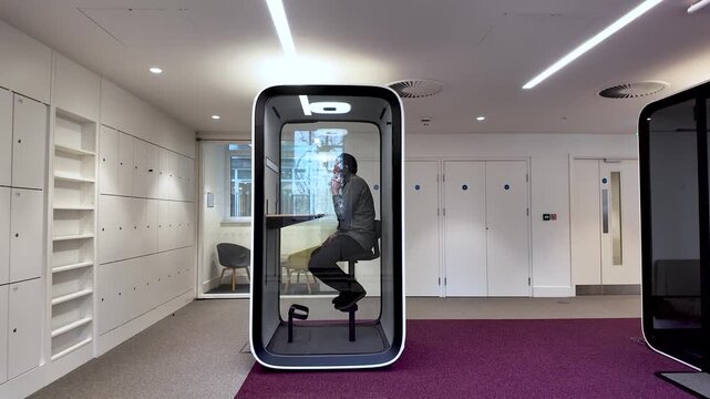 Man talking on phone inside transparent soundproof pod offering workspace privacy