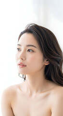 Naklejka premium Beautiful young Asian woman with clear skin and long dark hair looking thoughtfully to the side in soft natural light