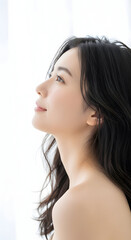 Fototapeta premium Serene young Asian woman with long dark hair looking upwards with a gentle expression and clean skin bathed in soft natural light, representing beauty and tranquility