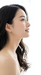 Fototapeta premium Beautiful young Asian woman with long dark hair in profile view with a gentle smile and looking upwards against a bright white background