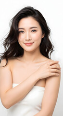 Fototapeta premium Beautiful young asian woman with long dark hair and clear skin smiling gently with her hand on her shoulder against a white background showcasing natural beauty and skincare