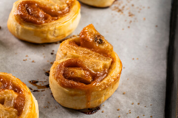 Freshly baked banana caramel puff pastry rolls on a baking sheet. Pastry. Dessert © Denis