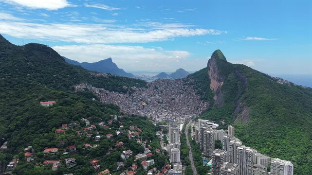 Rocinha favela during a sunny tropical day. Dense community nestled between lush green hills with Christ the Redeemer visible in the far distance. Long range forward aerial in 4K.