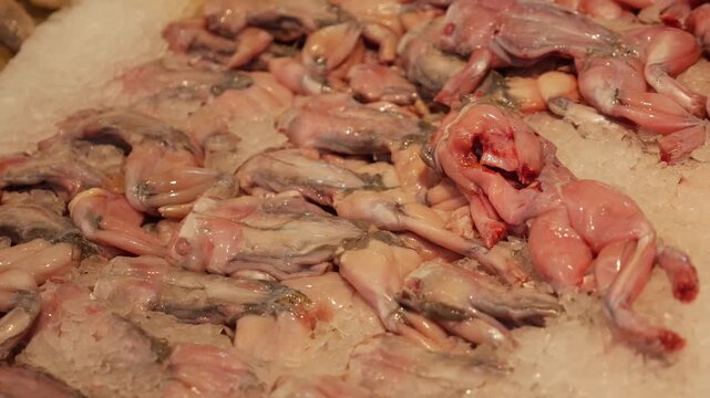 Skinned frogs are displayed on crushed ice in a supermarket seafood section, arranged on a chilled counter for sale. Exotic food market.