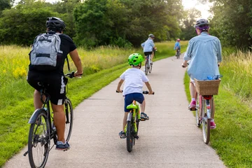 Fotobehang Wielersport Family children cycling paved countryside path green meadow trees during warm summer day light. Active outdoor lifestyle parenting recreation freedom childhood adventure healthy travel concept  © Kyryl Gorlov