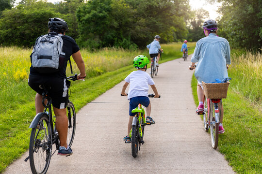 Family children cycling paved countryside path green meadow trees during warm summer day light. Active outdoor lifestyle parenting recreation freedom childhood adventure healthy travel concept