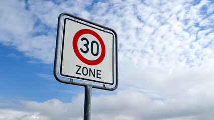 Road sign indicating a 30 zone speed limit against a backdrop of blue sky with scattered clouds © TatjanaMeininger